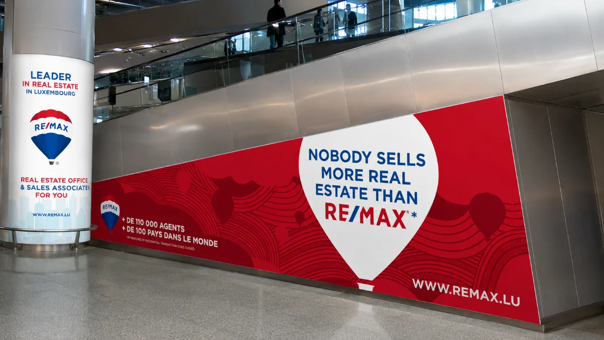 Supports RE/MAX Luxembourg : habillage mural rouge et totem de communication.